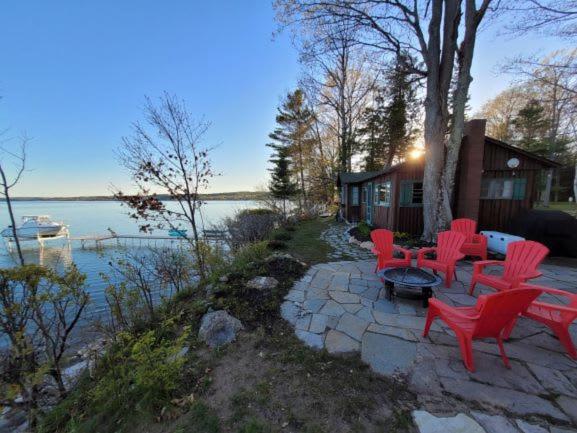 a patio with red chairs and a table next to a lake at Lee Point Classic Cabins on West Bay with Hot Tub in Suttons Bay