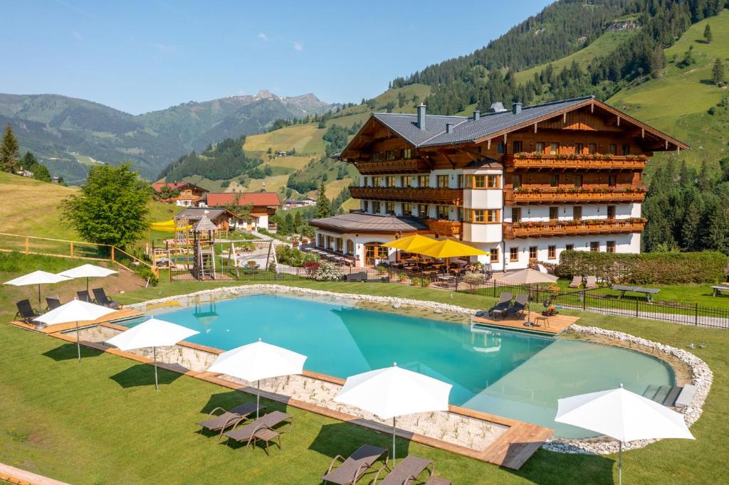 a hotel with a large swimming pool with chairs and umbrellas at Hotel Lammwirt in Grossarl