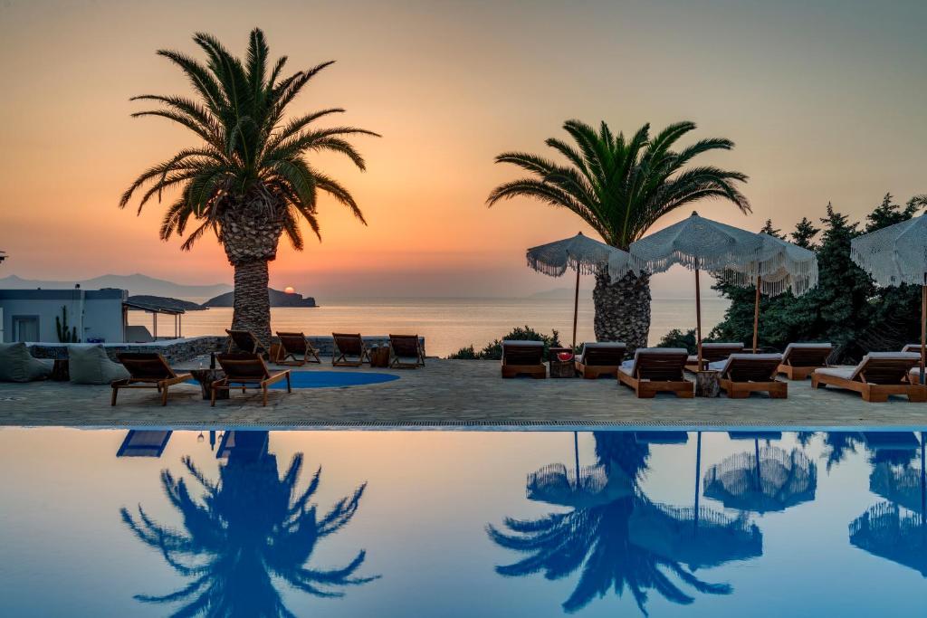 uma piscina com palmeiras e cadeiras e um pôr-do-sol em Faros Resort em Azolimnos