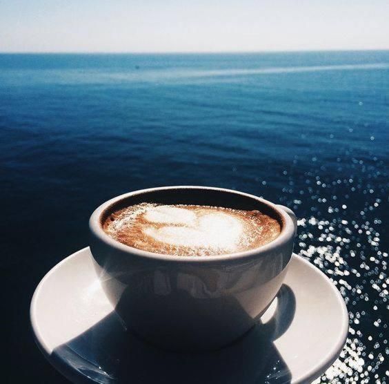a cup of coffee sitting on a plate next to the ocean at Comfortable apartment in Shëngjin