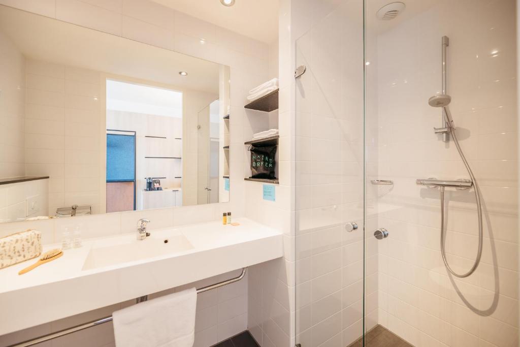La salle de bains blanche est pourvue d'un lavabo et d'une douche. dans l'établissement Hotel Casa Amsterdam, à Amsterdam