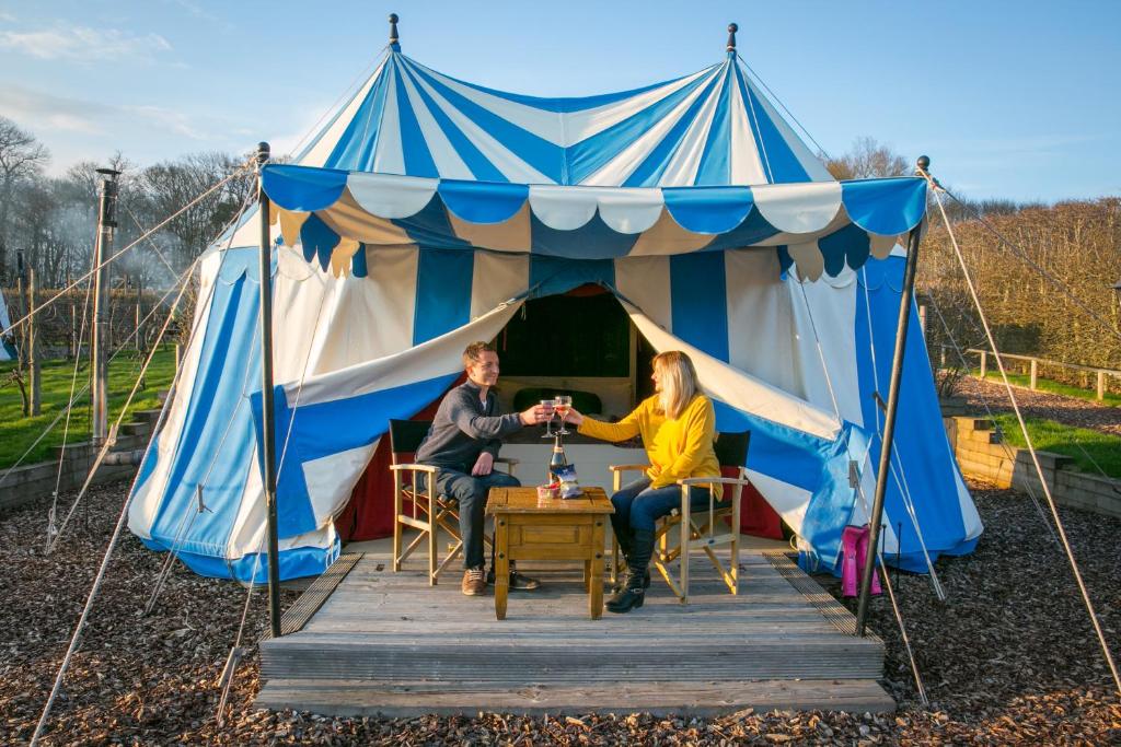 dwoje ludzi siedzących przy stole w niebiesko-białym namiocie w obiekcie Leeds Castle Knights Glamping w mieście Leeds