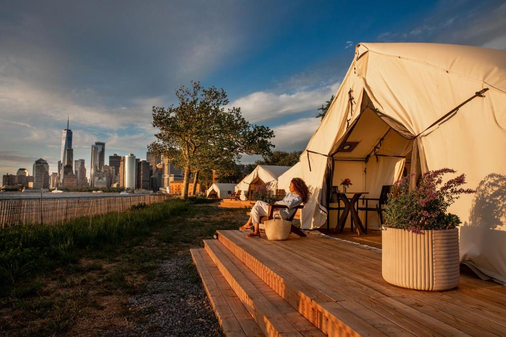 une grande tente avec une femme assise sur une terrasse en bois dans l'établissement Collective Governors Island, à New York