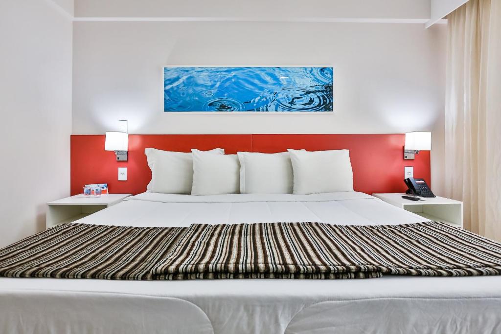 a bedroom with a large white bed with a red wall at Ramada Hotel & Suites Campos Pelinca in Campos dos Goytacazes