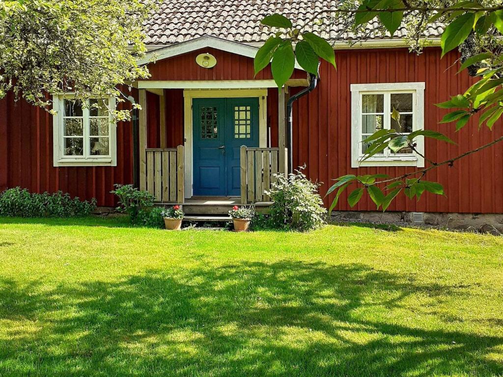 a red house with a blue door and a yard at 6 person holiday home in ALSTERBRO in Kättilstorp
