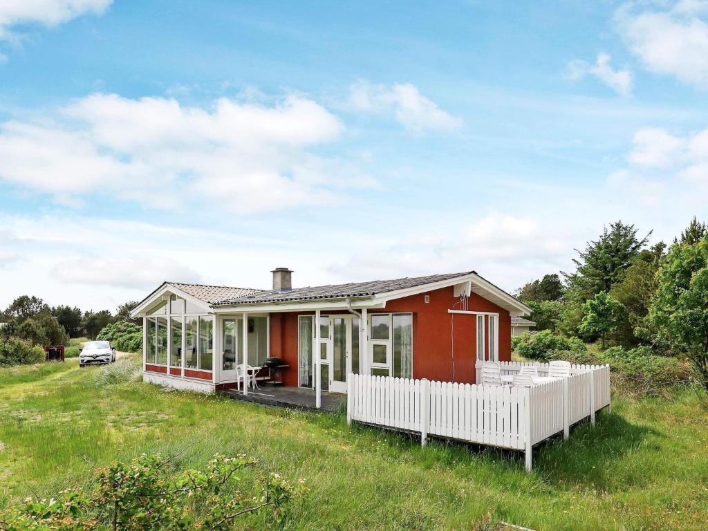 a red house with a white fence in a field at 5 person holiday home in Vejers Strand in Vejers Strand