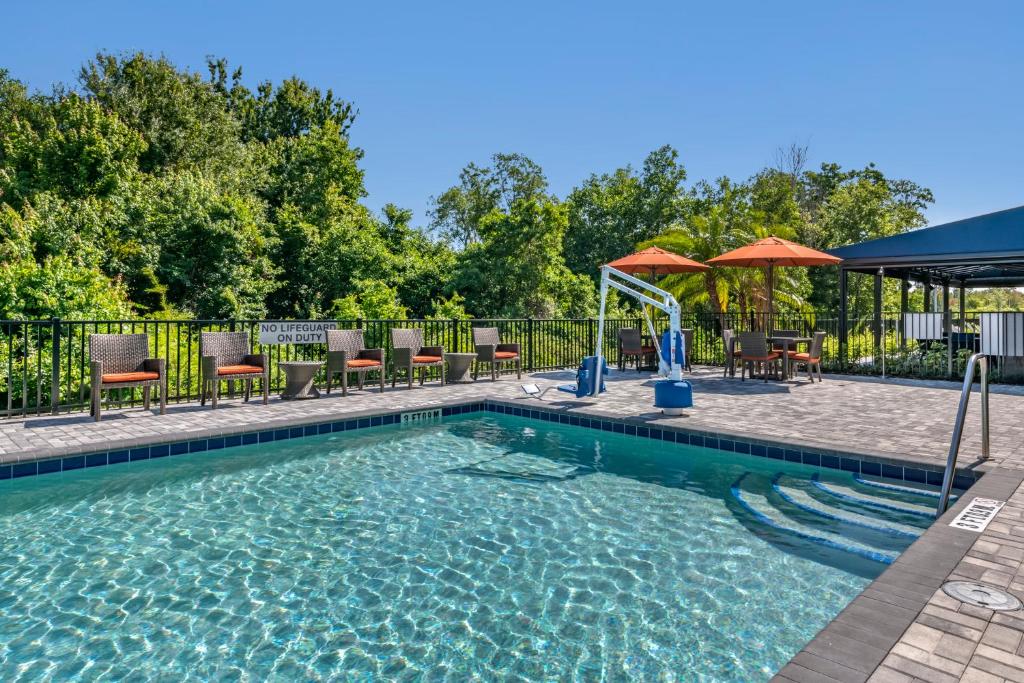 una piscina con sillas y sombrillas en un patio en Cambria Hotel Orlando Airport en Orlando