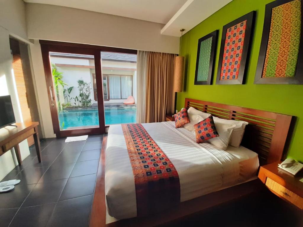 a bedroom with a bed with green walls and a pool at Gaing Mas Jimbaran Villas by Gaing Mas Group in Jimbaran