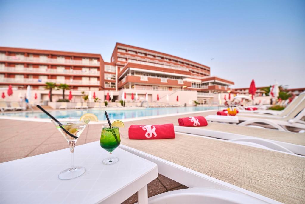 two glasses on a table next to a swimming pool at Hotel Albatros Plava Laguna in Poreč