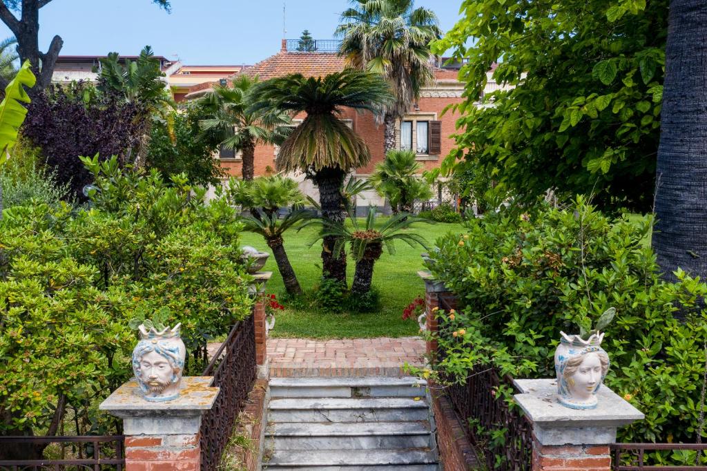 un giardino con due statue di volti su una recinzione di Villa dei Marchesi Carrozza a Santa Teresa di Riva