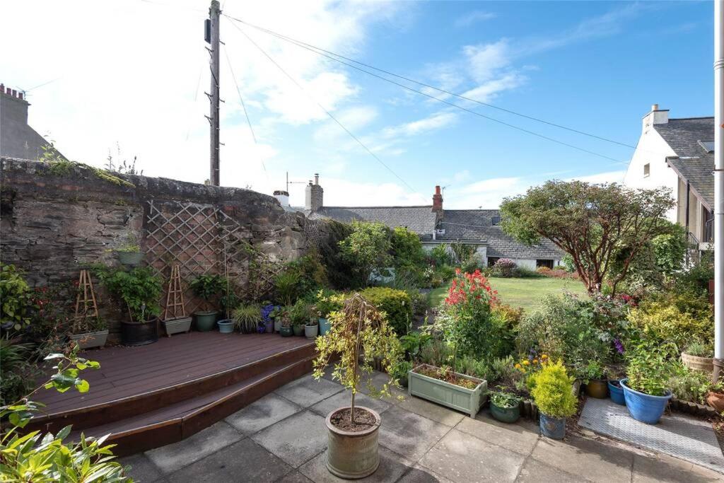 a garden with potted plants and a wooden bench at The Colours Riverside apartment with garden in Broughty Ferry