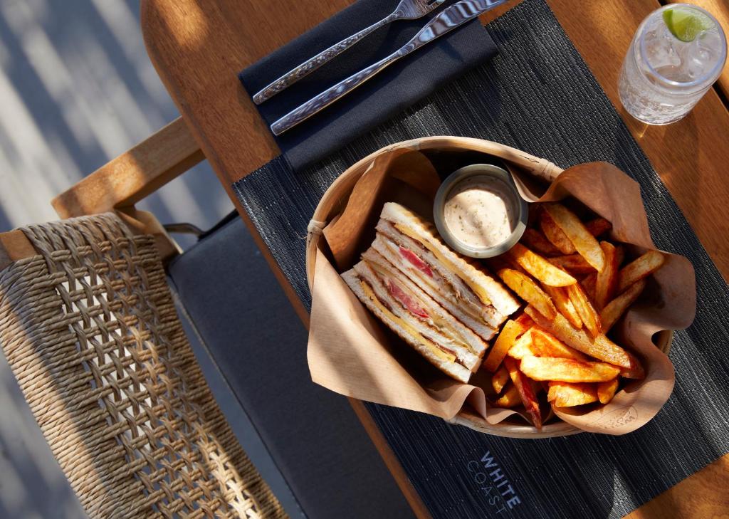 a sandwich and chips on a table with dipping sauce at Domes White Coast Milos, Adults Only - Small Luxury Hotels of the World in Mytakas