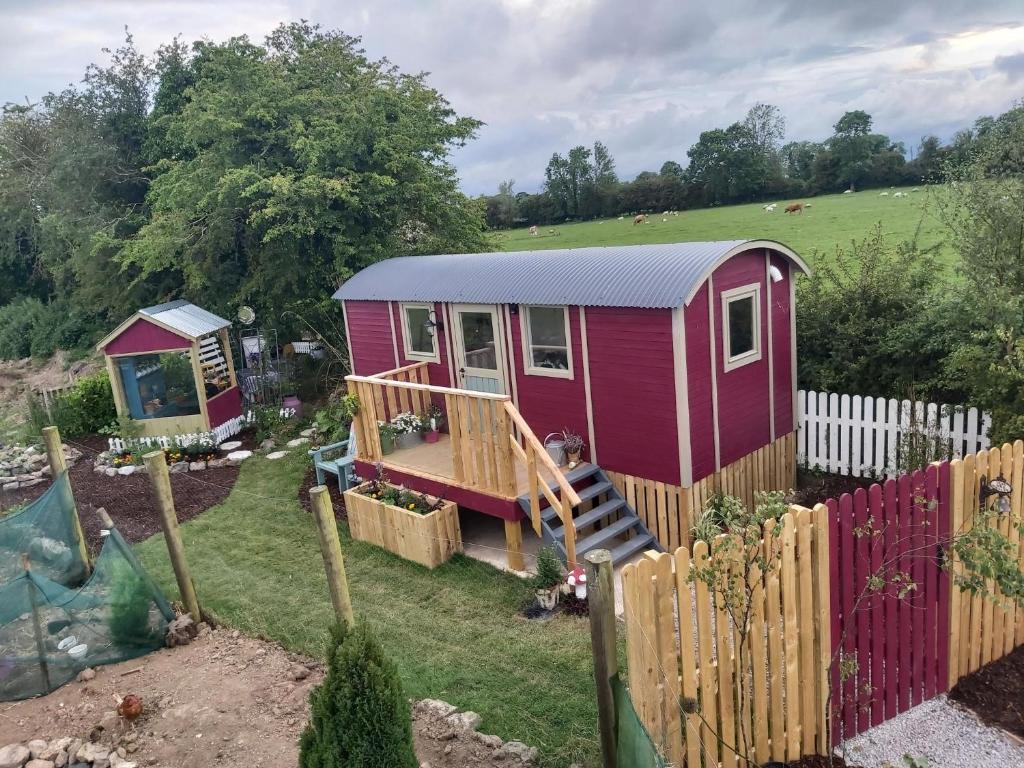 a red tiny house in a yard with a fence at The Feathers Shepherds Hut in Áth Eascrach