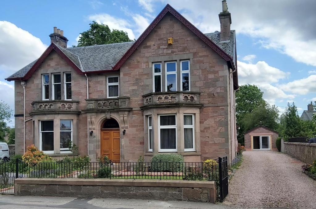 una vieja casa de ladrillo con una valla en una entrada en Glencoe House Inverness en Inverness