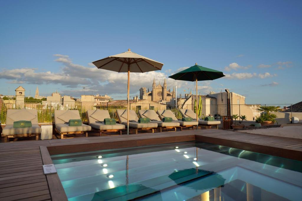 una piscina con sillas y sombrillas en la azotea en Can Bordoy Grand House & Garden, en Palma de Mallorca