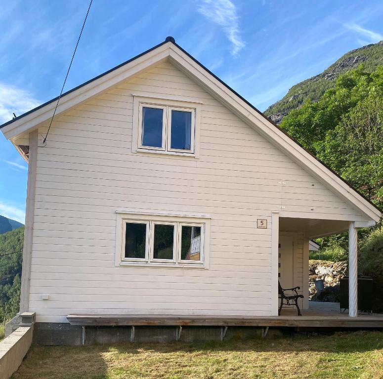 une maison blanche avec une terrasse couverte et des montagnes en arrière-plan dans l'établissement Indreli feriehus, à Flåm