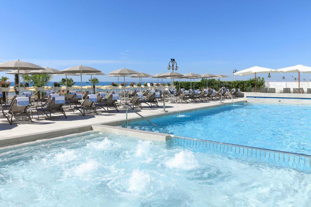 a large swimming pool with chairs and umbrellas at Hotel Cavalieri Palace in Lido di Jesolo