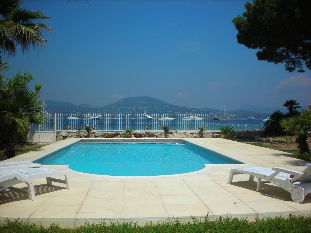 a swimming pool with two white chairs and the ocean at Villa Playa del Sol - B2 in Saint-Tropez