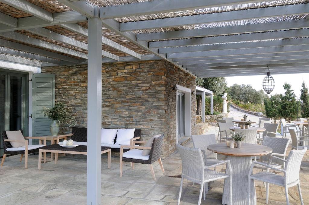 a patio with white chairs and tables and a wooden pergola at Aegea Blue Cycladic Resort in Zorgos 