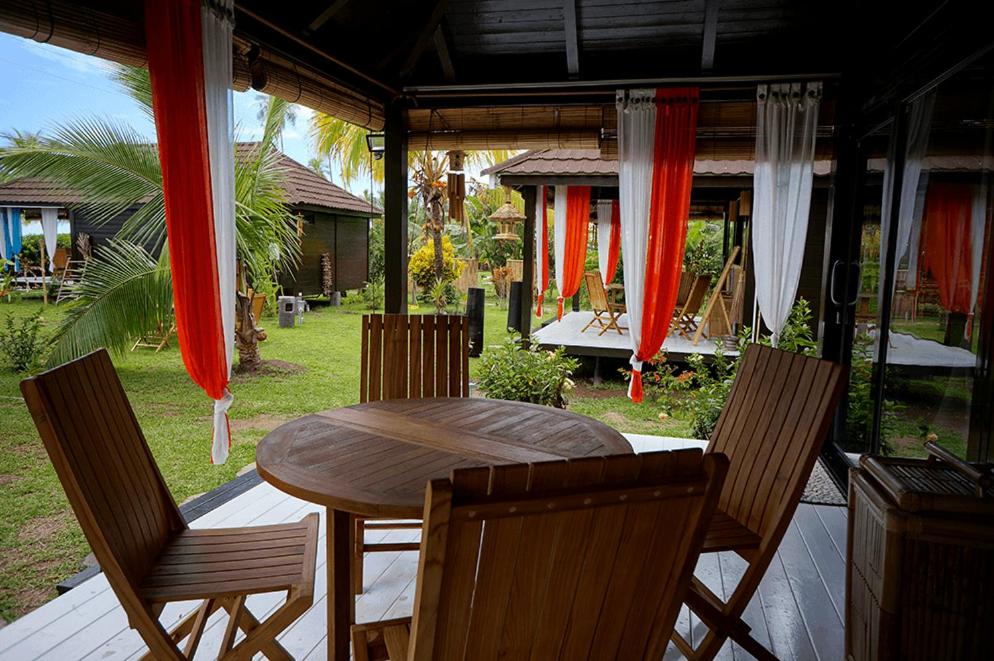 einen Holztisch und Stühle auf einer Veranda mit roten Vorhängen in der Unterkunft La Perle Tahaa in Tapu' amu