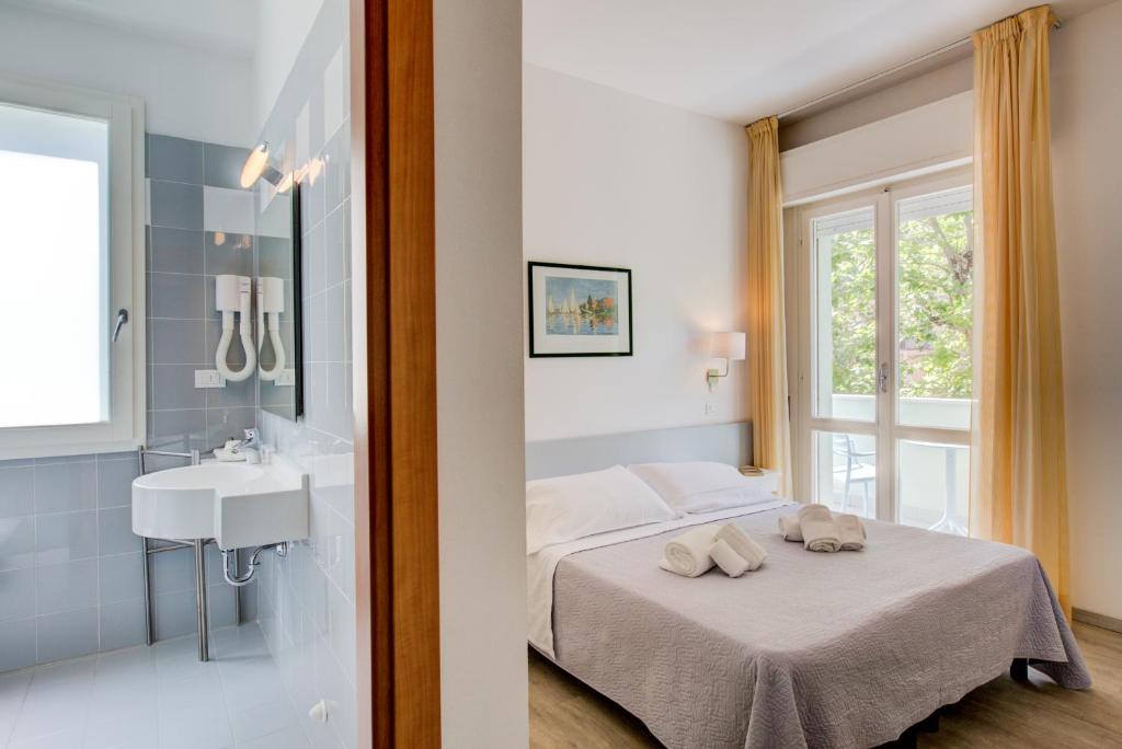 a bedroom with a bed and a sink and a window at Hotel Ivano in Rimini