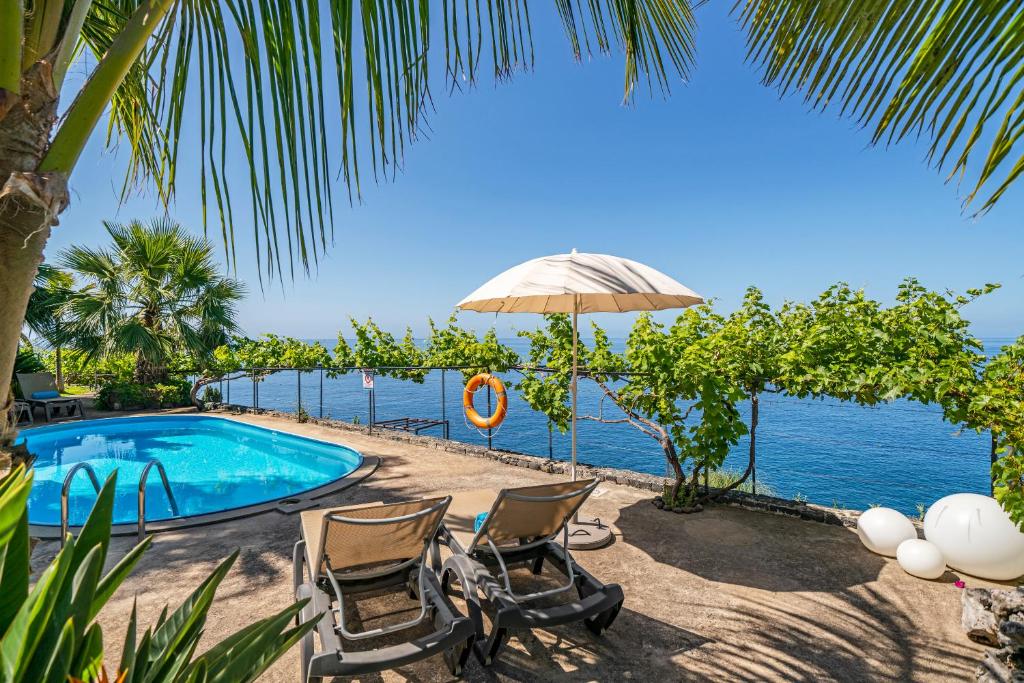 a pool with chairs and an umbrella and the ocean at Quinta Golfinho in Arco da Calheta