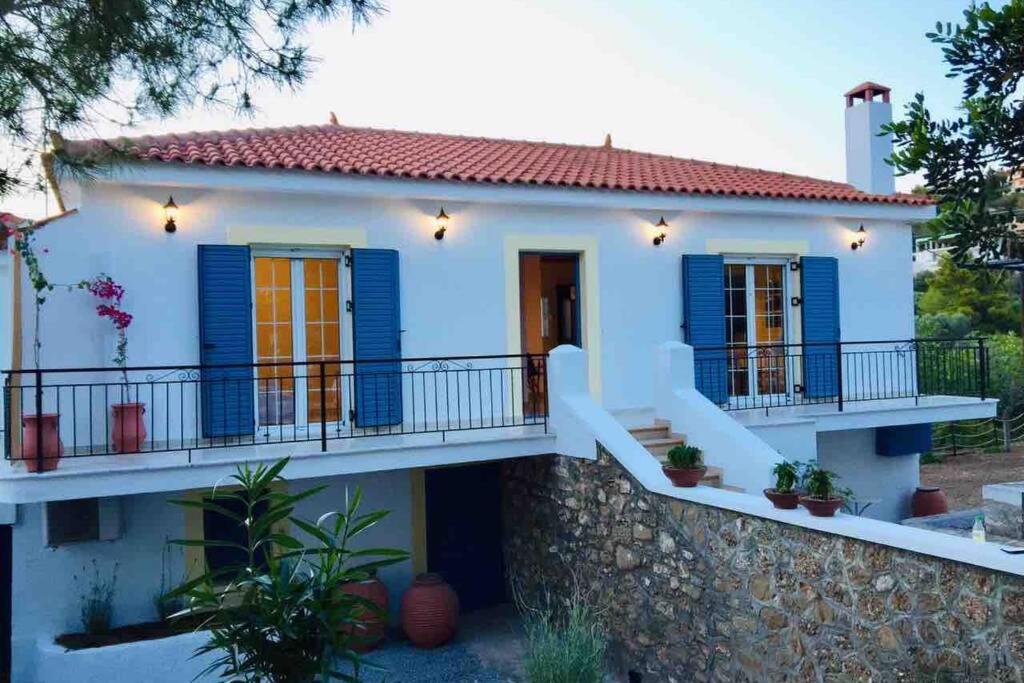 una casa con persianas azules y una pared de piedra en Gerani Maison Agios Aimilianos beautiful view en Porto Heli