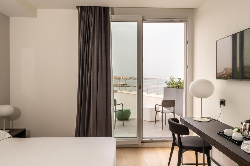 a hotel room with a bed and a desk and a balcony at Hotel Punta Tipa in Trapani