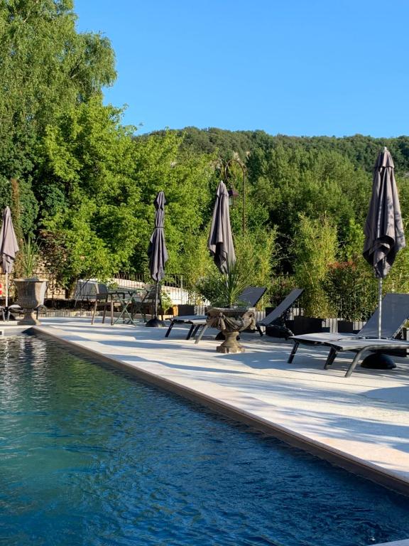 uma piscina com guarda-sóis, mesas e cadeiras em Les appartements d artiste de la Villa du 15 - Restaurant La Maison - piscine chauffée em Les Eyzies-de-Tayac