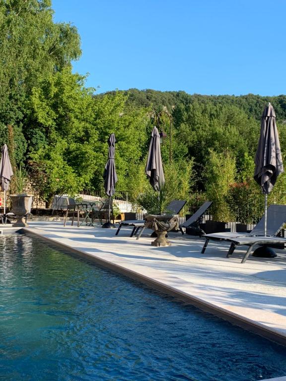 a swimming pool with umbrellas and tables and chairs at Les appartements d artiste de la Villa du 15 - Restaurant La Maison - piscine chauffée in Les Eyzies-de-Tayac