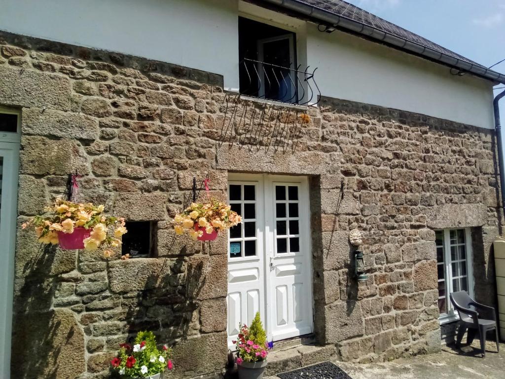 a stone house with a white door and flowers in front at Gite L'insinière in Saint-Martin-de-Chaulieu