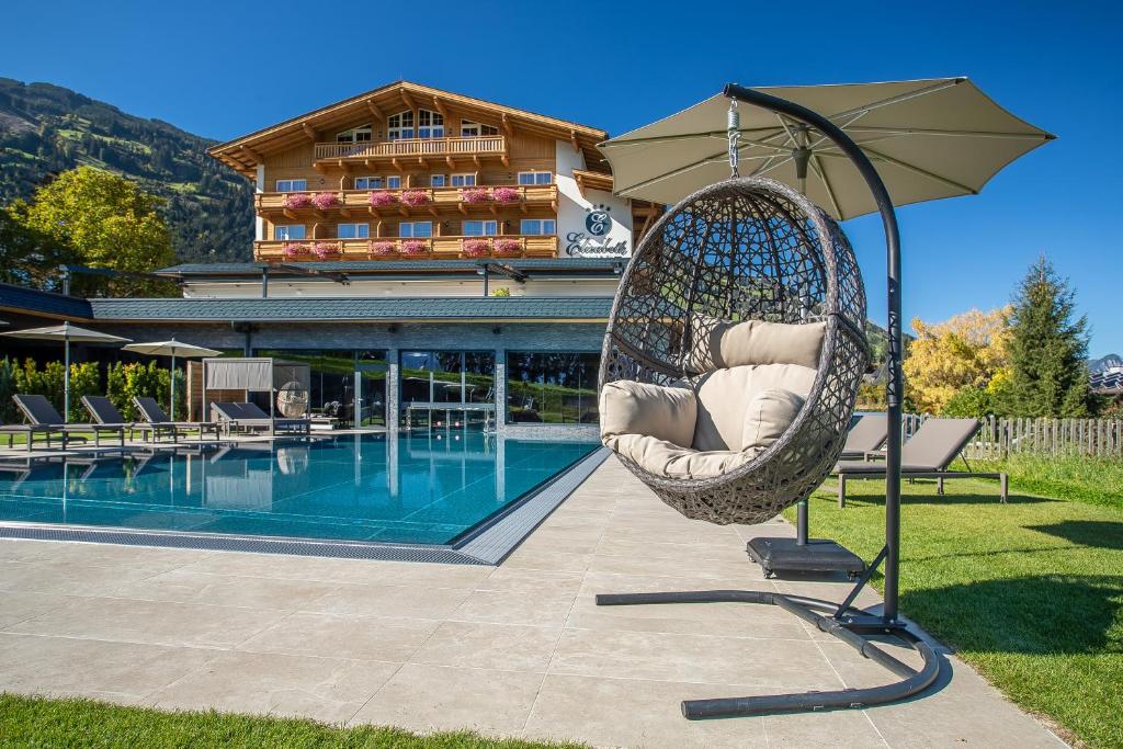 a hanging chair with an umbrella next to a pool at Hotel Elisabeth in Fügen