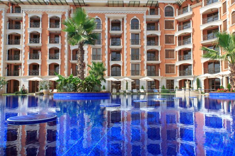 a large building with palm trees and a large swimming pool at Cascadas Ravda in Ravda