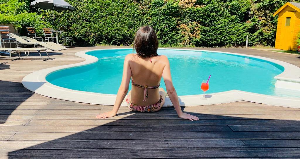 a woman in a bikini sitting next to a swimming pool at Hotel Villa Cinzia in Villanova Mondovì