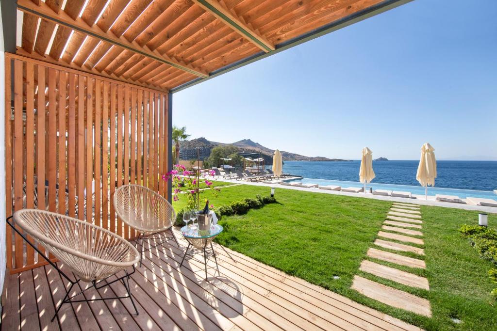 a wooden deck with chairs and a table and the ocean at niXie Hotel & Beach - Adult Only in Yalıkavak