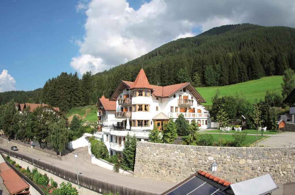 ein großes weißes Haus mit einer Steinmauer und einem Berg in der Unterkunft Turmhotel Gschwendt in Gsieser Tal