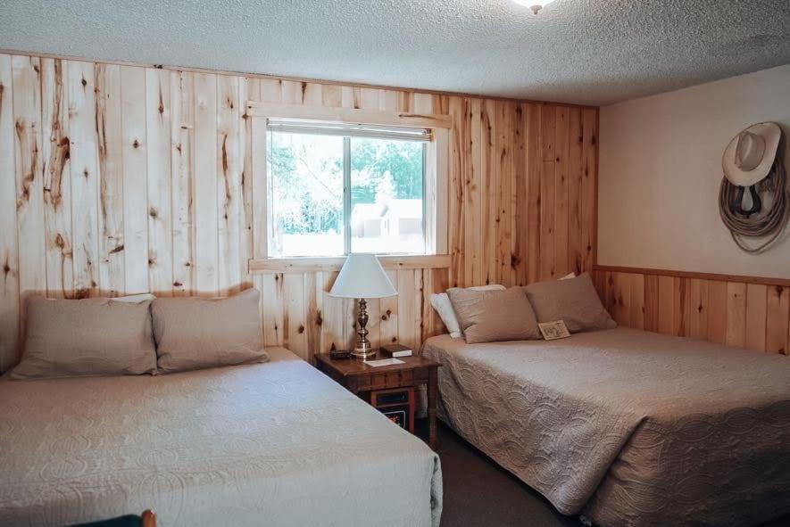 two beds in a room with wooden walls and a window at Circle K Ranch in Rico