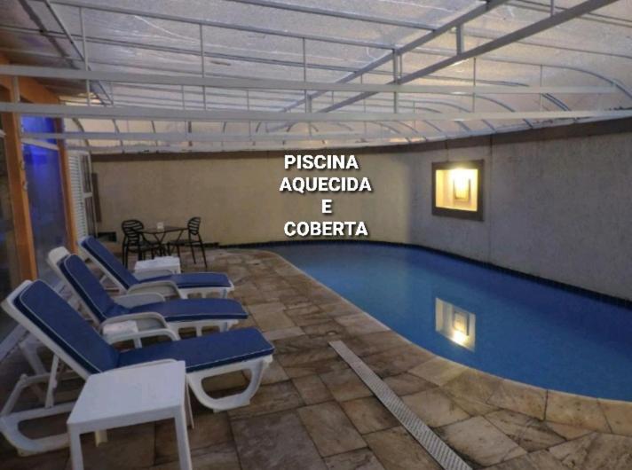 a swimming pool with blue chairs and a sign at Hotel Costa Balena-Piscina Aquecida Coberta in Guarujá