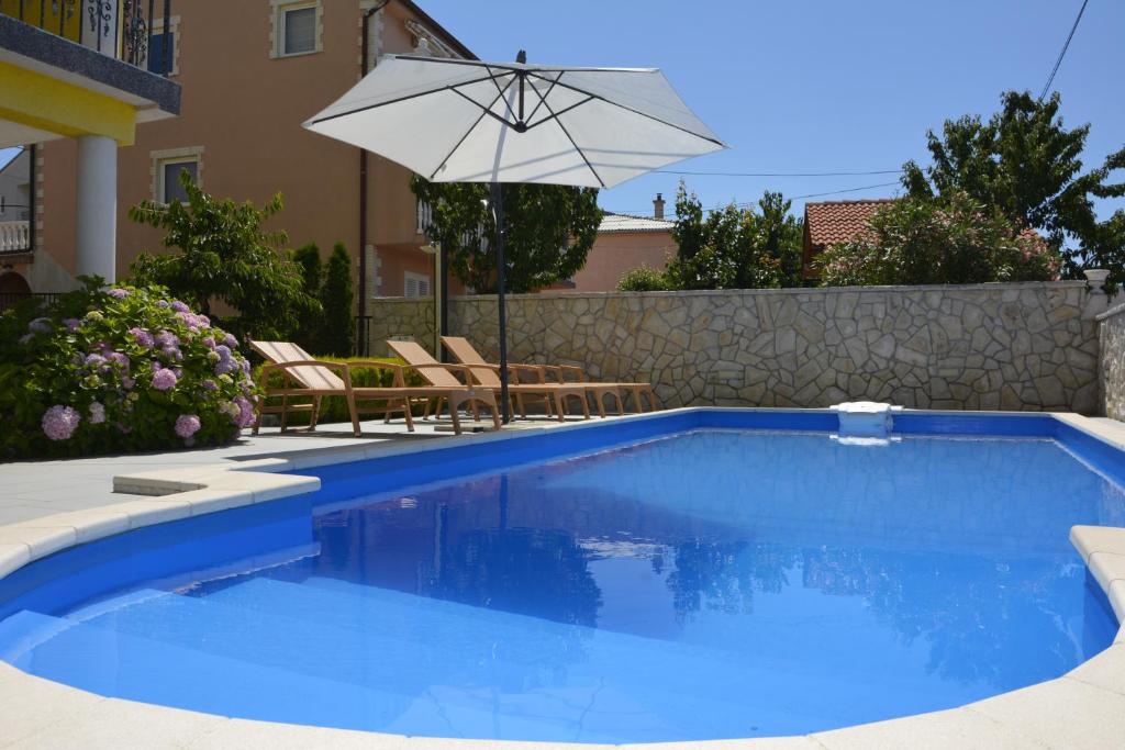 a blue swimming pool with an umbrella and chairs at Apartman 2 in Senj