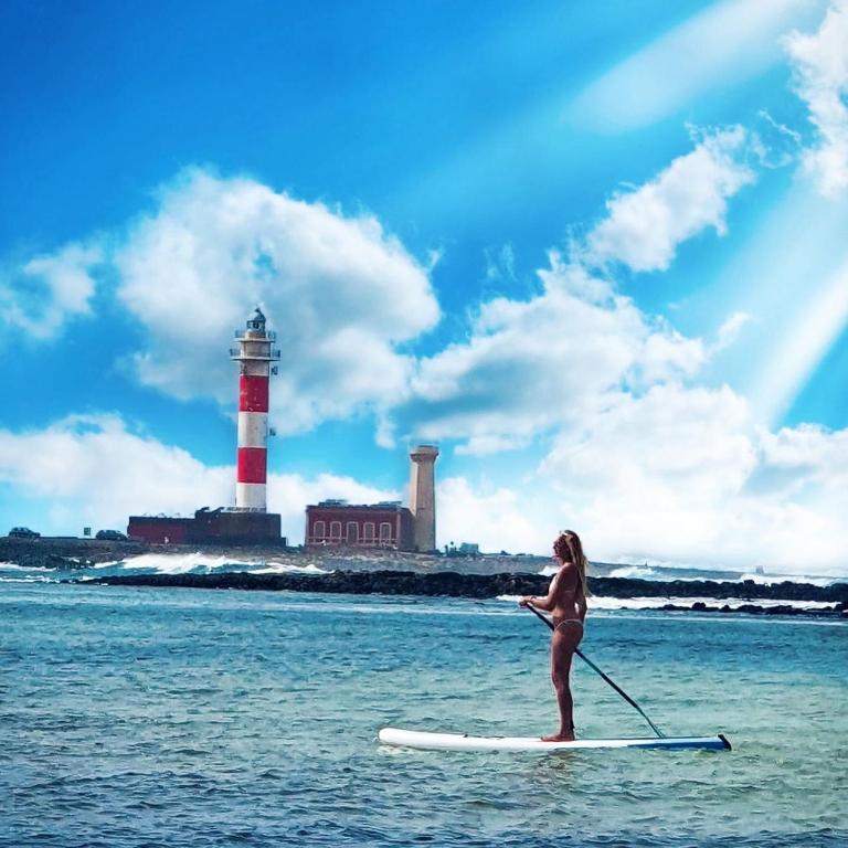 a woman on a paddle board in the water with a lighthouse at Olas de Lobos in Corralejo