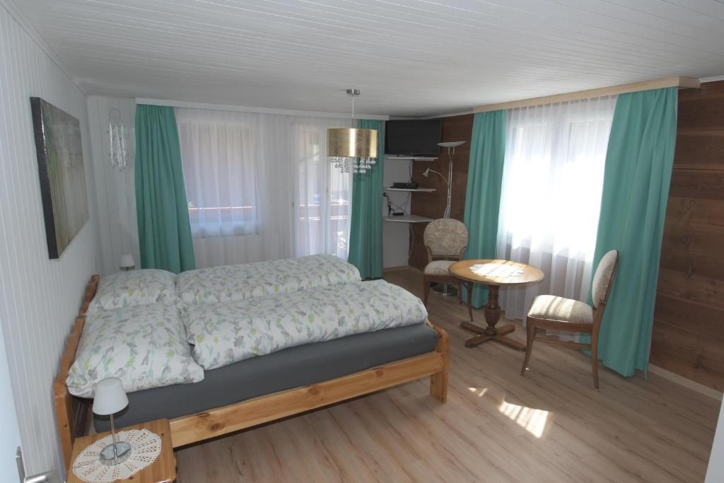 1 dormitorio con 1 cama con cortinas verdes y mesa en Haus Wiedersehen, Mischabel (2-Zi) en Saas-Grund