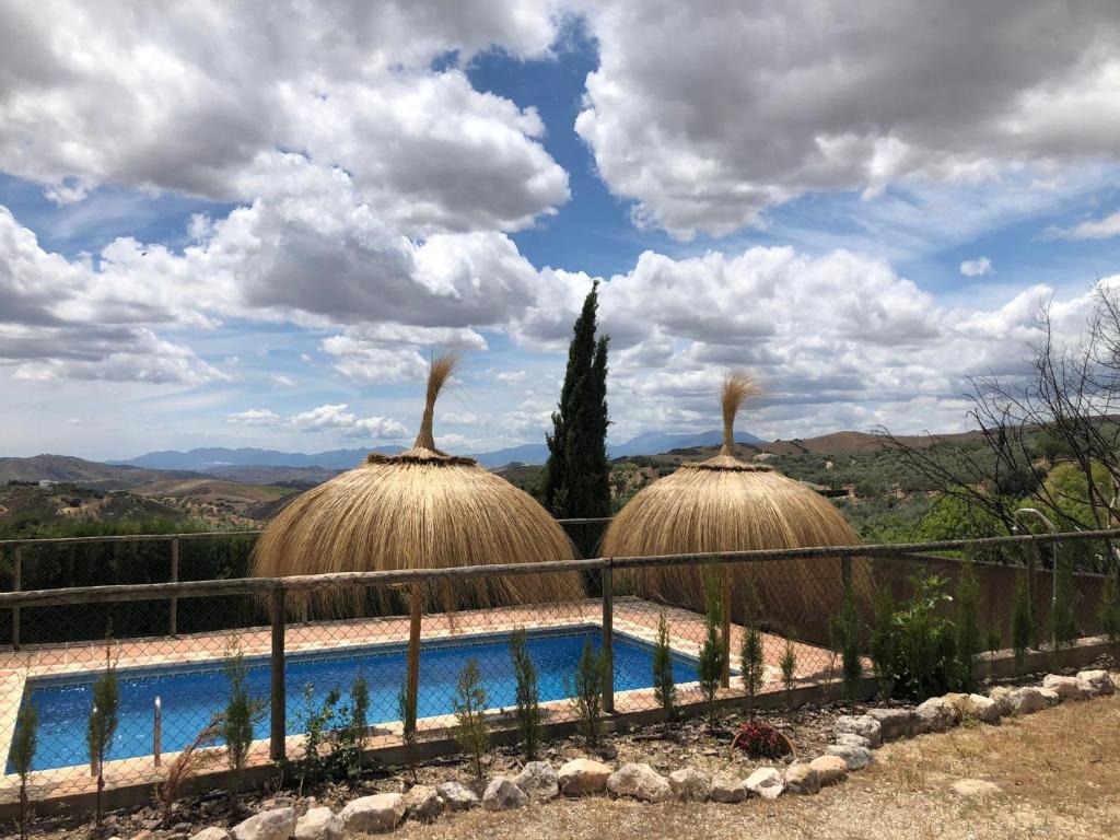 un resort con piscina e due capanne di paglia di Casa Rural La Higuera Chica a Málaga