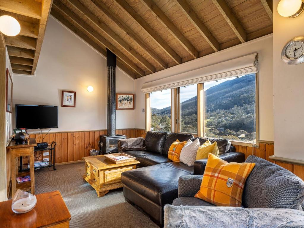 a living room with a leather couch and a large window at Banjo 4 Two Bedroom with Loft real fireplace and mountain views in Thredbo