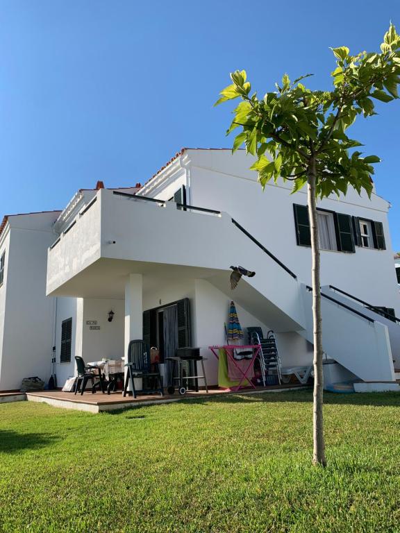 ein weißes Haus mit einem Baum im Hof in der Unterkunft Ca la Marta apartamento con piscina y jardín a 150m de la playa in Arenal d'en Castell