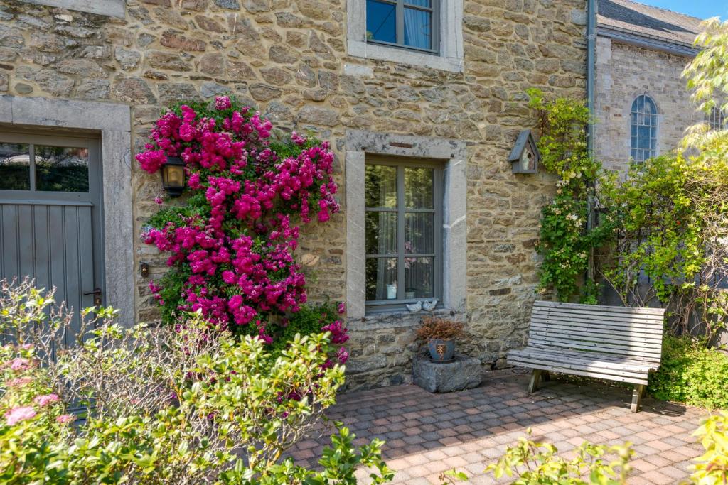 una casa de piedra con un banco y flores rosas en La Renardière - Chanly, en Wellin