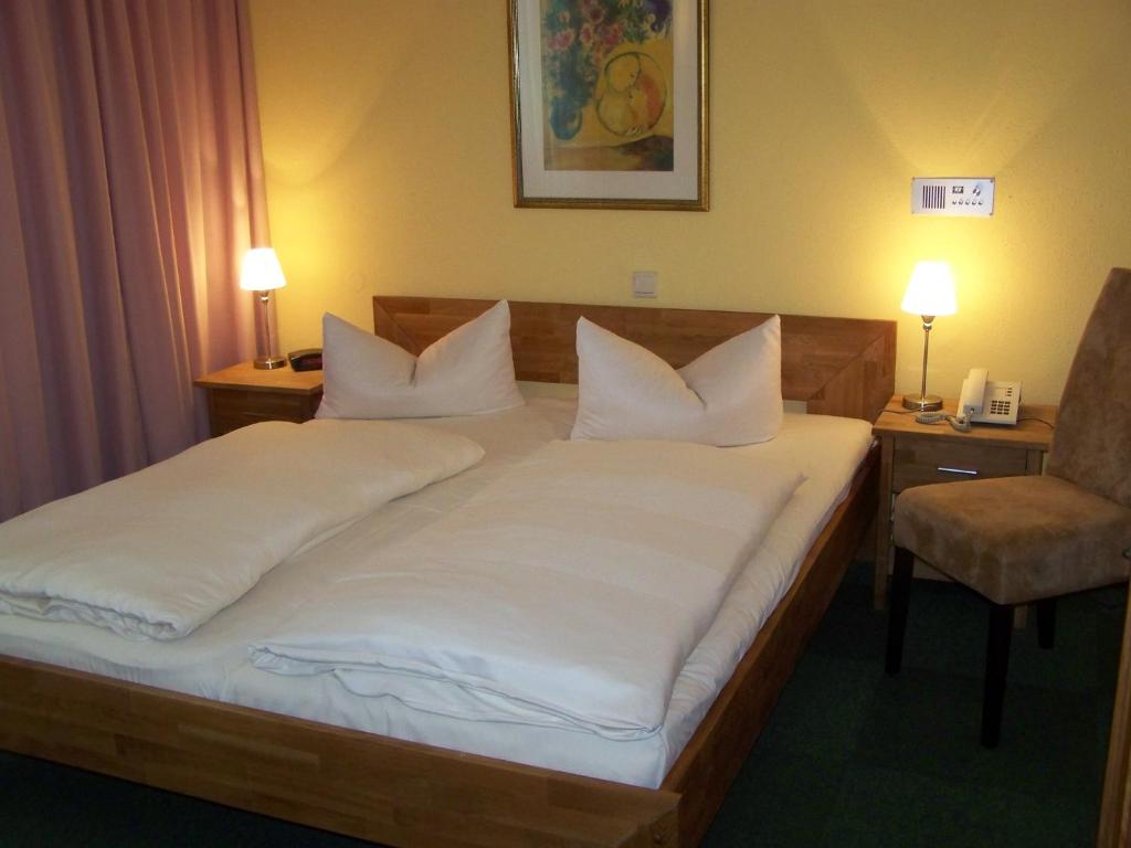 a bedroom with a bed with white pillows and a chair at Hotel Am Stiftsberg in Aschaffenburg