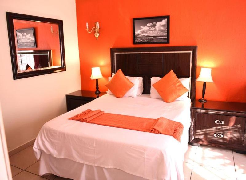 1 dormitorio con 1 cama grande y paredes de color naranja en Chancellors Court Guest House en Pretoria