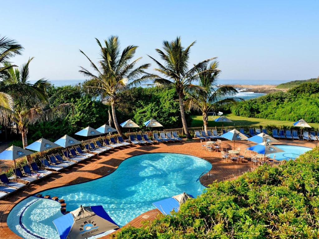 a resort with a pool and chairs and palm trees at Pumula Beach Hotel in Umzumbe