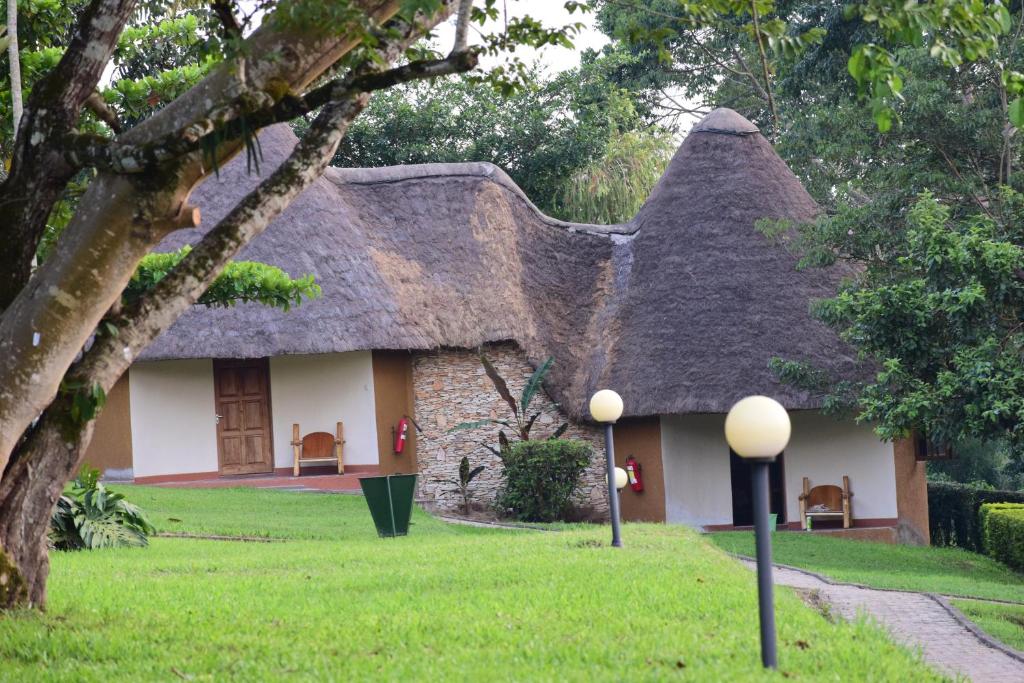 una casa con tetto di paglia e sedie in cortile di Kibale Guest Cottages a Fort Portal