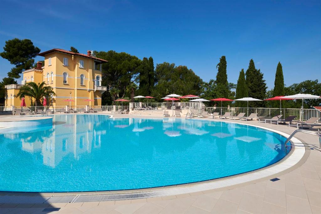 a large swimming pool with chairs and umbrellas at Apartments Bellevue Plava Laguna in Poreč